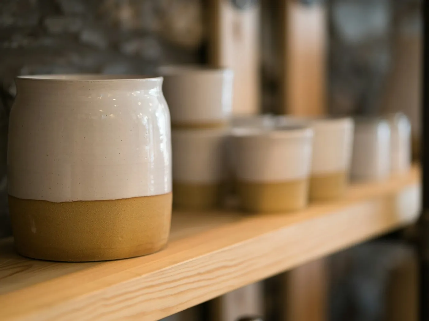 Reihe glasierter, zweifarbiger Becher auf einem Holzregal in der Werkstatt